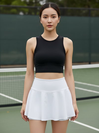 Model wearing a black sleeveless cropped top and white athletic skort on a tennis court with a net in the background.