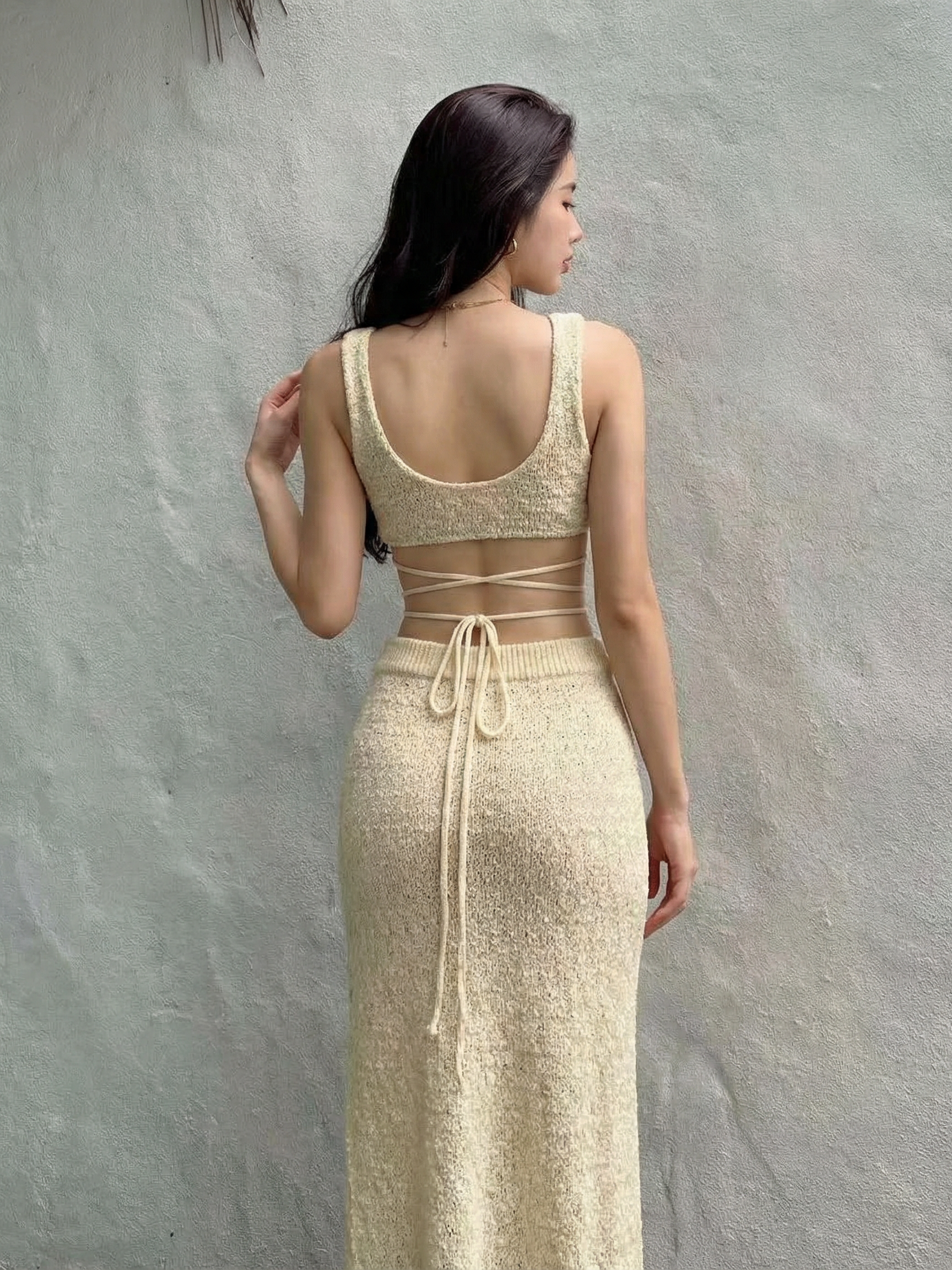 Back view of a woman in a beige crochet bikini top with wide straps and lace-up back, paired with a matching long crochet skirt.