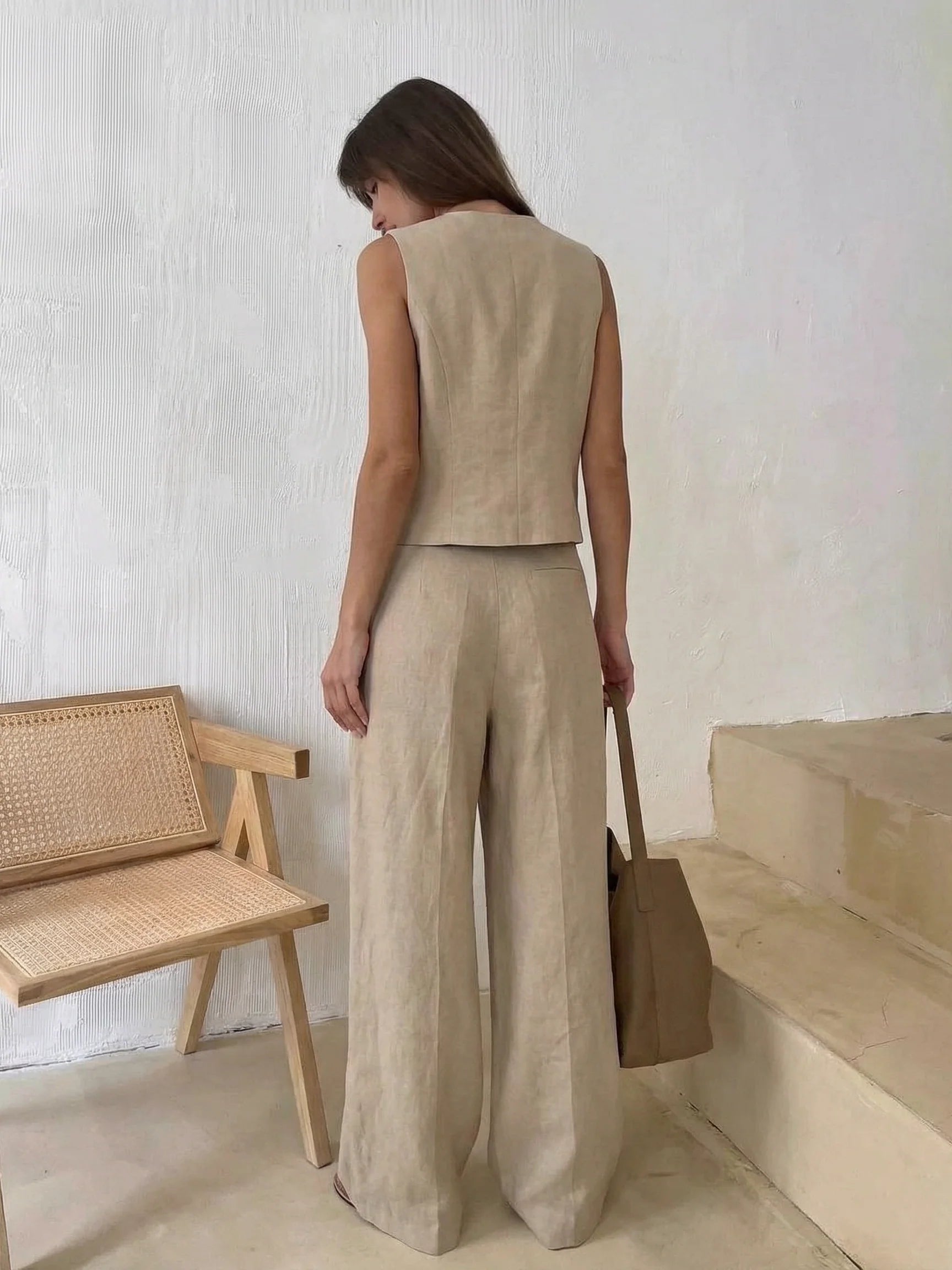 Beige sleeveless vest with cropped waistcoat over wide-leg linen trousers; back view of a woman carrying a brown tote.