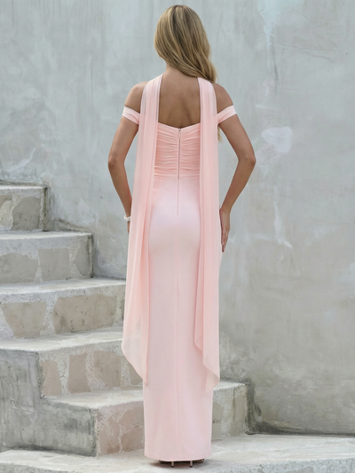 Back view of a soft pink off-shoulder maxi dress with long draped scarf detail, standing on stone steps.