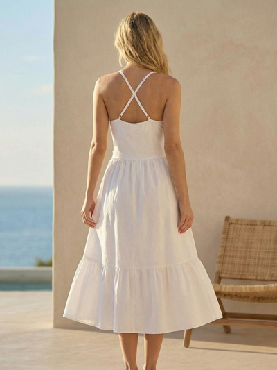 Back view of a white halter-neck midi dress with crisscross straps and a tiered skirt, worn by a woman by the sea.