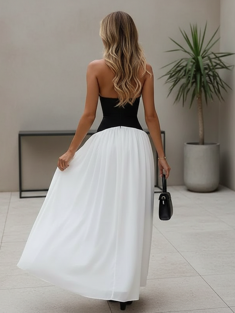 Back view of a woman in a two-tone halter corset maxi dress with a black bodice and white skirt, blonde hair.