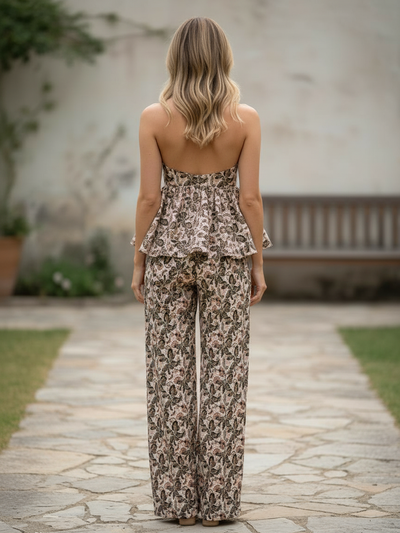 Back view of a woman in a beige boho leaf-print halter peplum top with matching wide-leg pants, on a stone path.