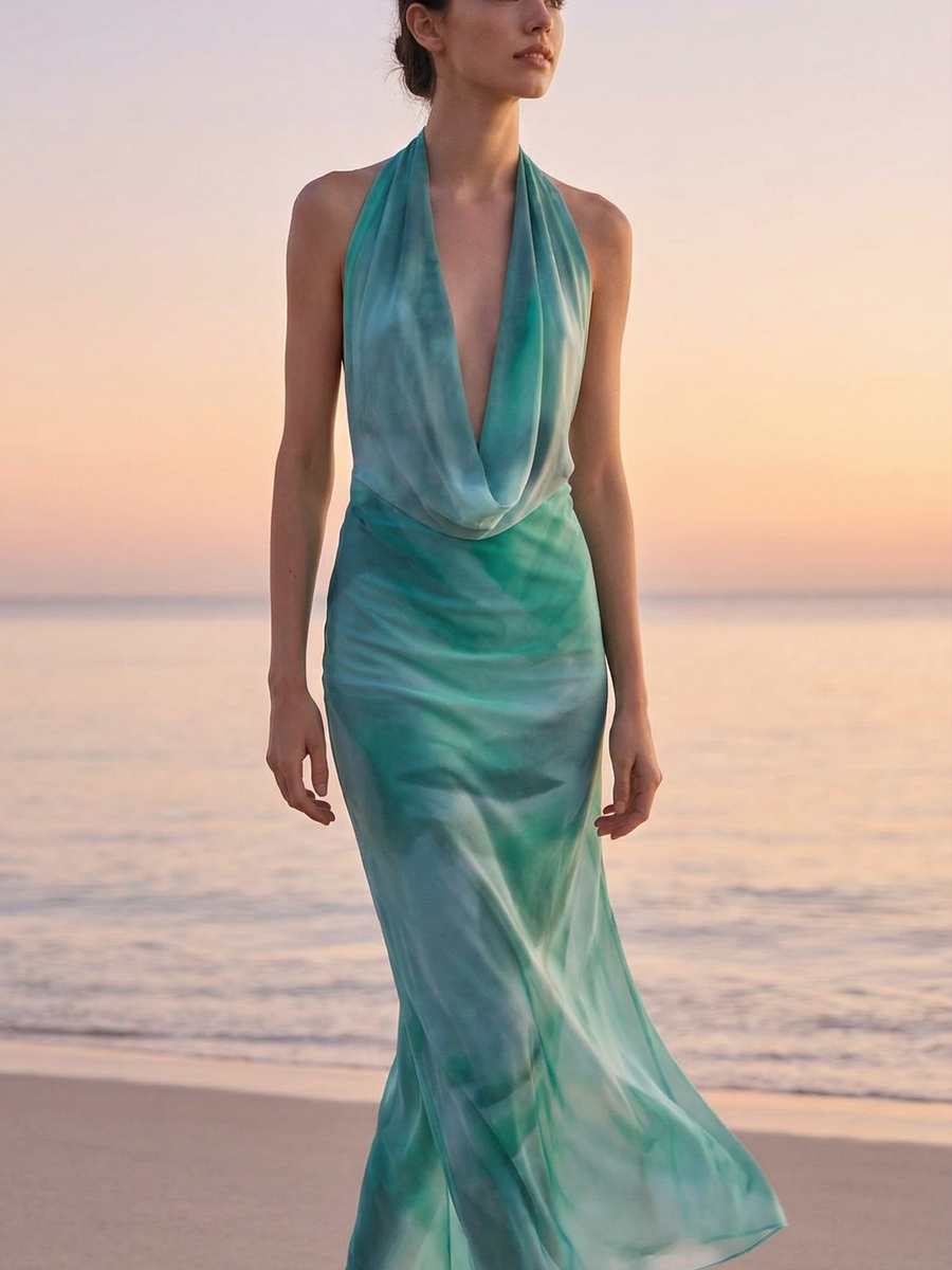 Woman on a beach in a teal-to-green ombre halter cowl-neck maxi dress, flowing down to the sand.