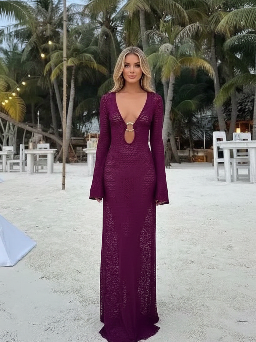 Woman on a sandy beach wearing a deep purple crochet maxi cover-up with bell sleeves and an O-ring cut-out at the bust