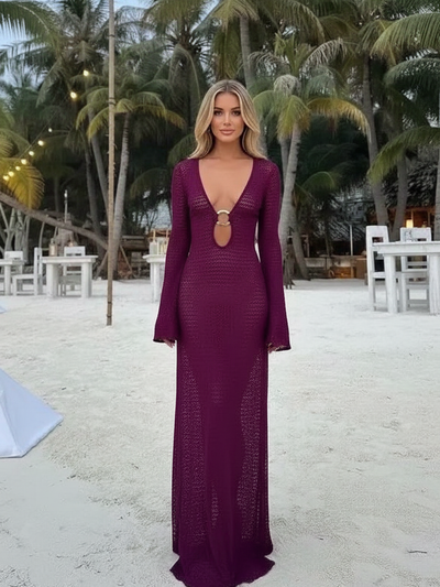 Woman on a sandy beach wearing a deep purple crochet maxi cover-up with bell sleeves and an O-ring cut-out at the bust
