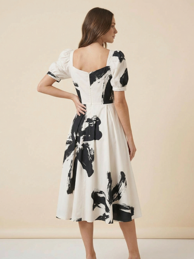 Back view of a white midi dress with black-and-white tie-dye print; corset-style bodice, puff sleeves, A-line skirt.