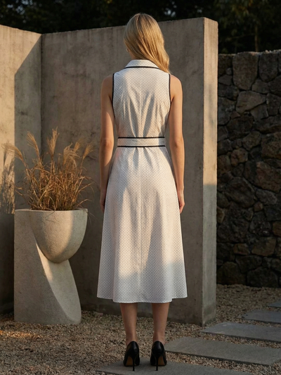 Back view of sleeveless beige polka-dot shirt midi dress with black piping at collar and belt, worn with black heels.