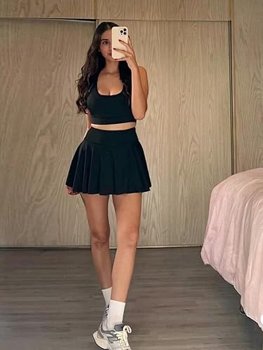 Woman wearing a black crop top and layered black skort, white socks, gray sneakers, posing in a mirror selfie.