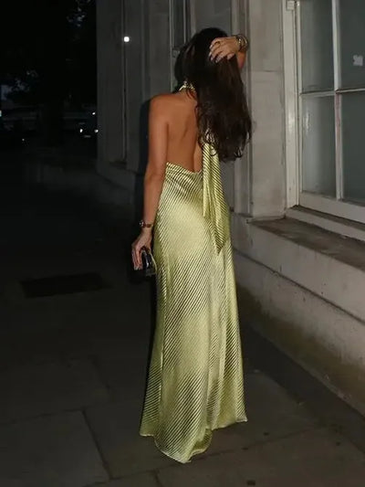 Backless halter-neck striped maxi dress in pale lime, knot at back, model with dark hair on street holding a clutch.
