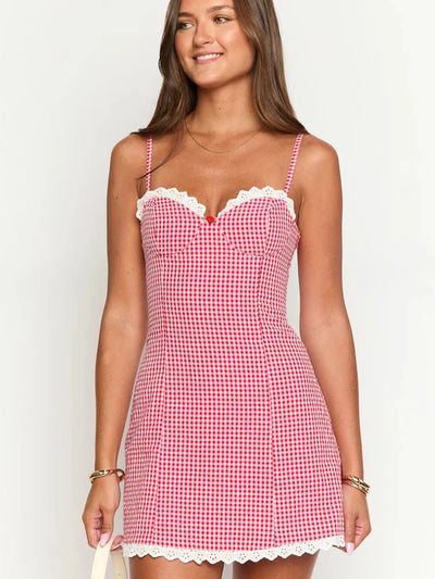 Red gingham mini dress with adjustable spaghetti straps and white lace trim at bust and hem, worn by a smiling model.