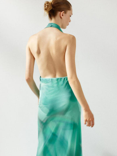 Back view of a model wearing a teal ombre halter-neck satin maxi dress with an open back and flowing fabric.