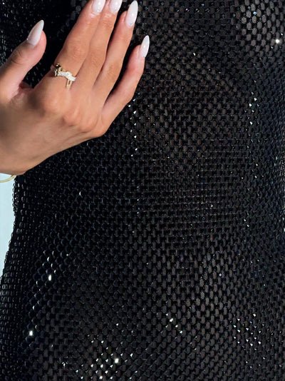 Close-up of a hand with long white manicured nails wearing a gold ring, resting on a black square-sequin dress.