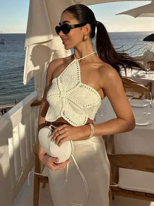 Ivory crochet butterfly halter crop top on a woman by the seaside, wearing sunglasses, satin skirt, and a white purse.