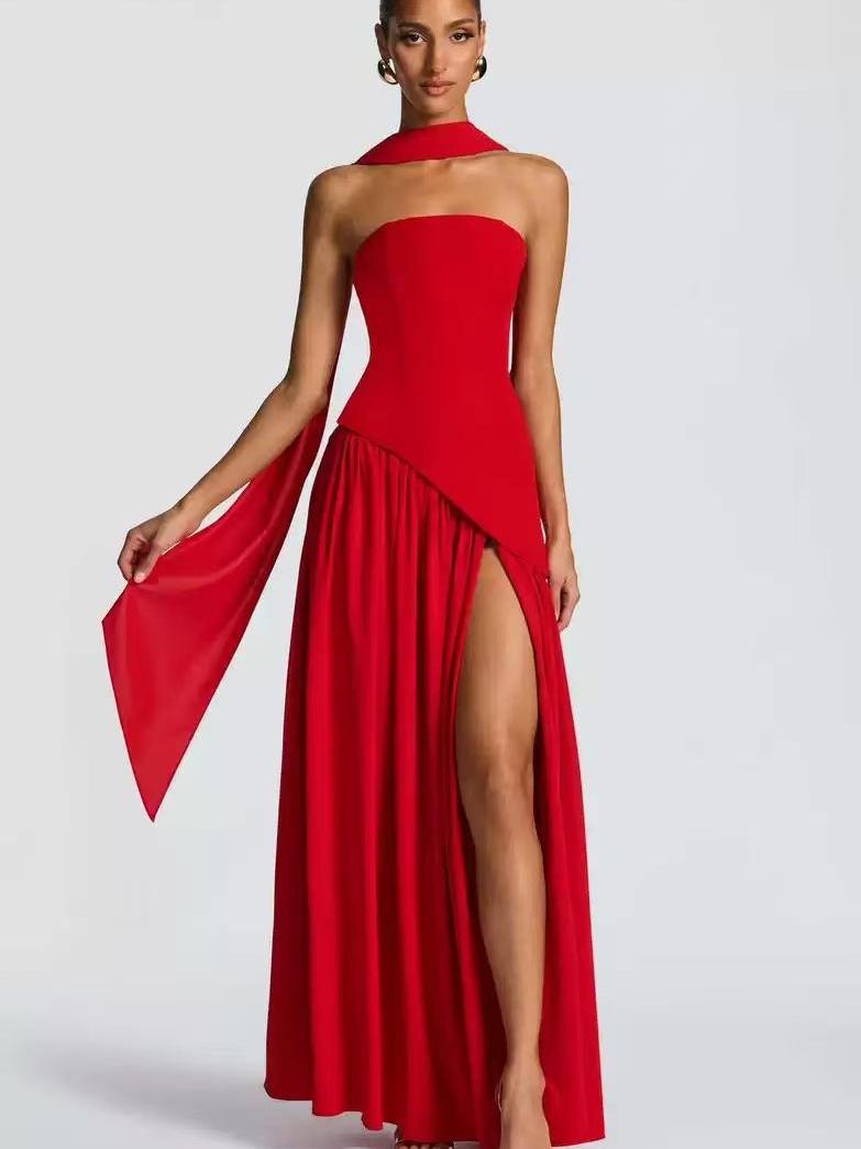 Red high-slit asymmetric tube maxi dress with diagonal overlay and scarf neckpiece, open-toe sandals.