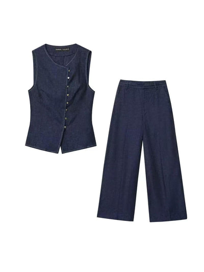Dark indigo denim sleeveless waistcoat with button-down front and curved hem, paired with matching wide-leg trousers.
