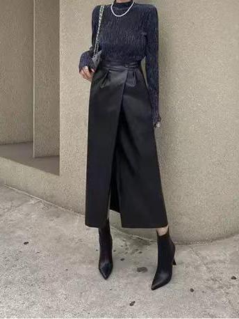 Black faux leather wrap-front midi skirt with waist tie, paired with a dark navy knit top and chain-strap bag.