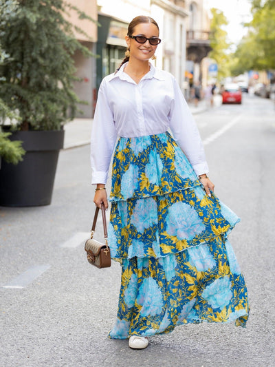 City street scene: woman in white blouse wearing a blue and yellow floral print, tiered georgette maxi skirt.