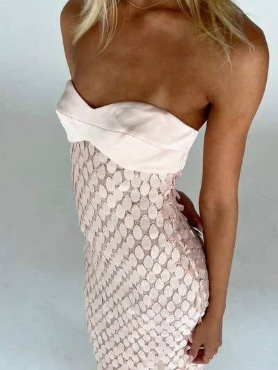 Side view of a strapless pale pink mermaid-scale sequin tube maxi dress with a white folded satin bust overlay.