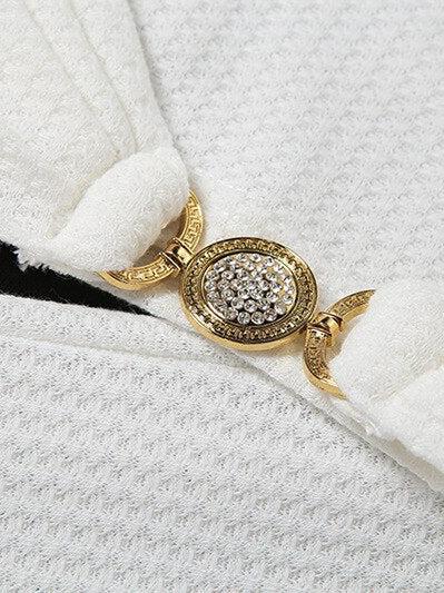 Close-up of white textured fabric with a gold oval ring encrusted with crystals resting on it