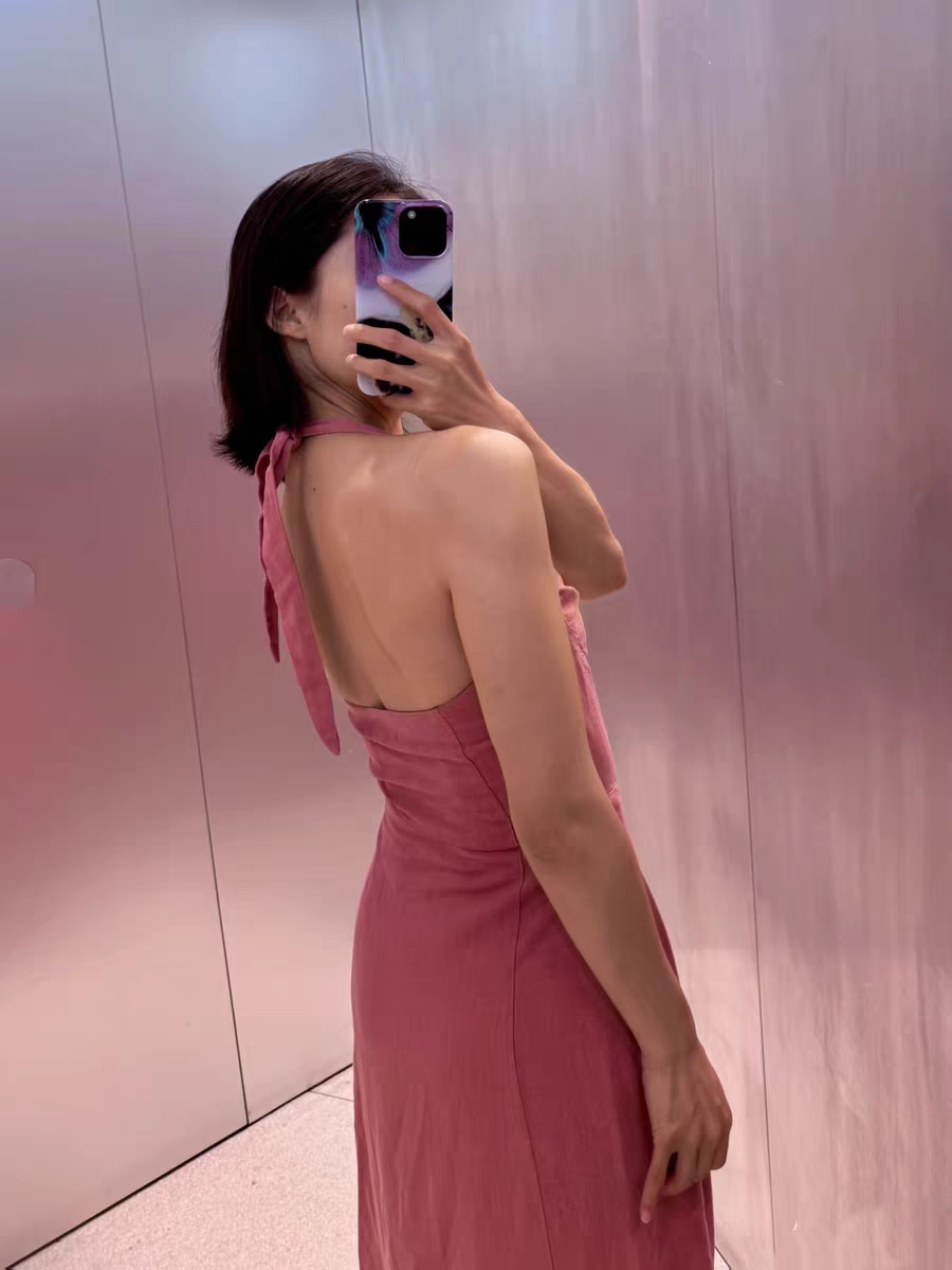 Pink halter-neck backless maxi dress with neck tie and fitted waist, shown from the side in a mirror selfie.