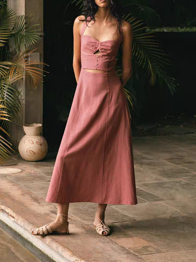 Woman in pink halter-neck cut-out maxi dress with button bodice and A-line skirt, beige sandals, garden backdrop.