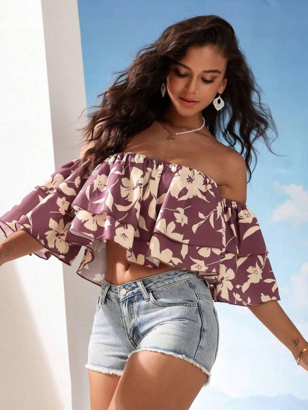 Model in mauve floral off-shoulder crop top with double ruffles, paired with light-wash denim shorts against a blue sky.