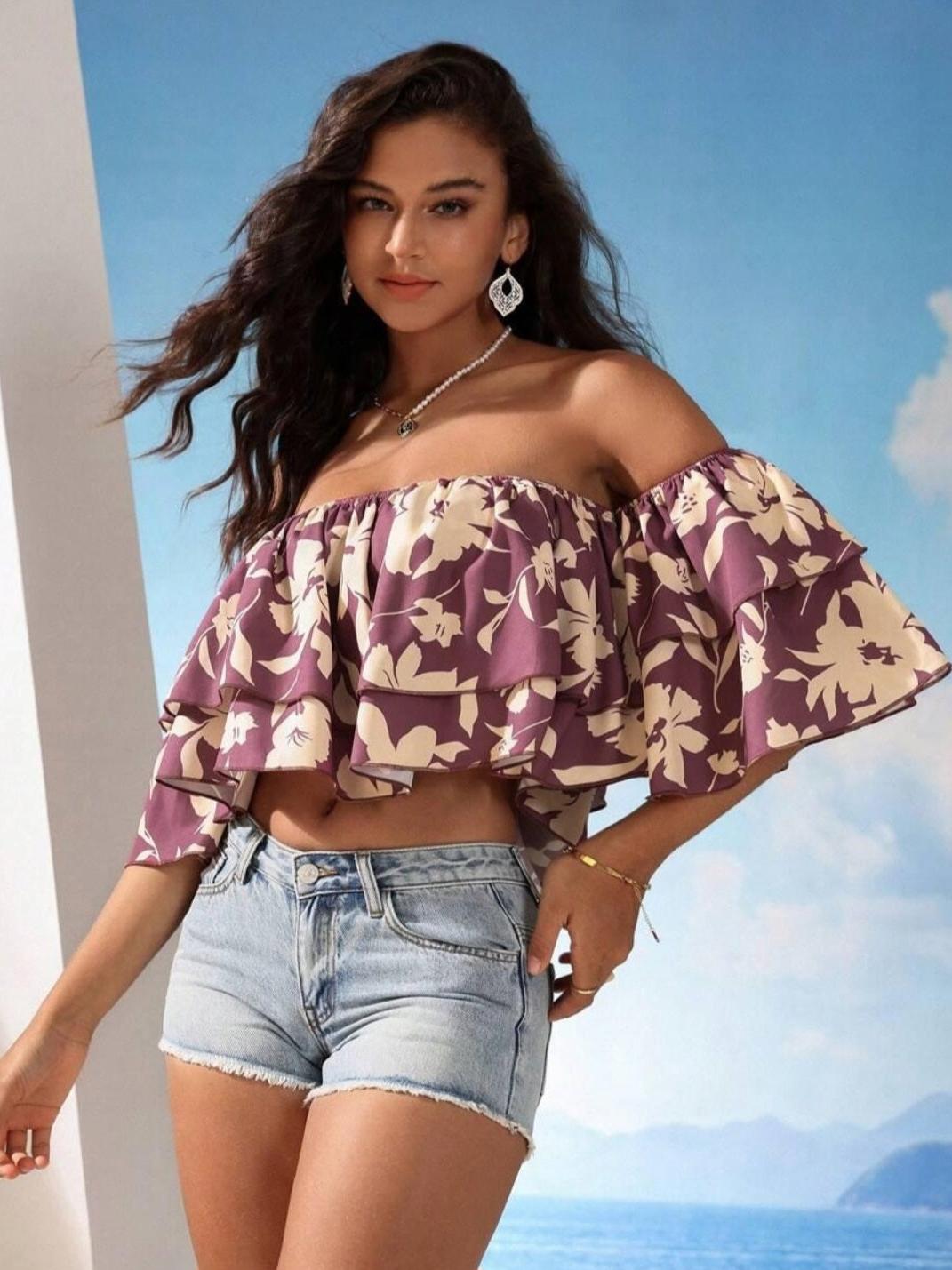 Woman wearing mauve floral off-shoulder two-tier ruffle crop top and light denim shorts against a blue sky backdrop