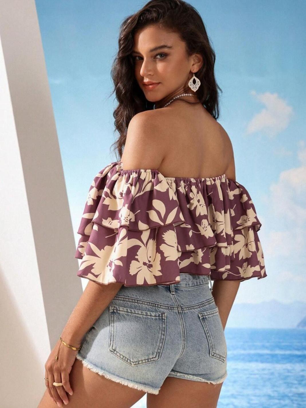 Woman wearing purple floral off-shoulder crop top with double-layer ruffle, paired with light denim shorts.