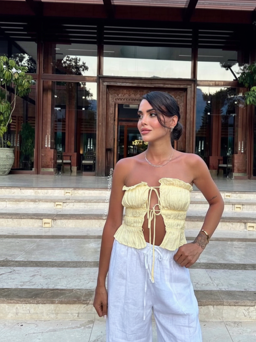 Whimsy Ruffle Cropped Top by Exclusives; yellow strapless tank with front tie and peplum ruffles, paired with white pants.