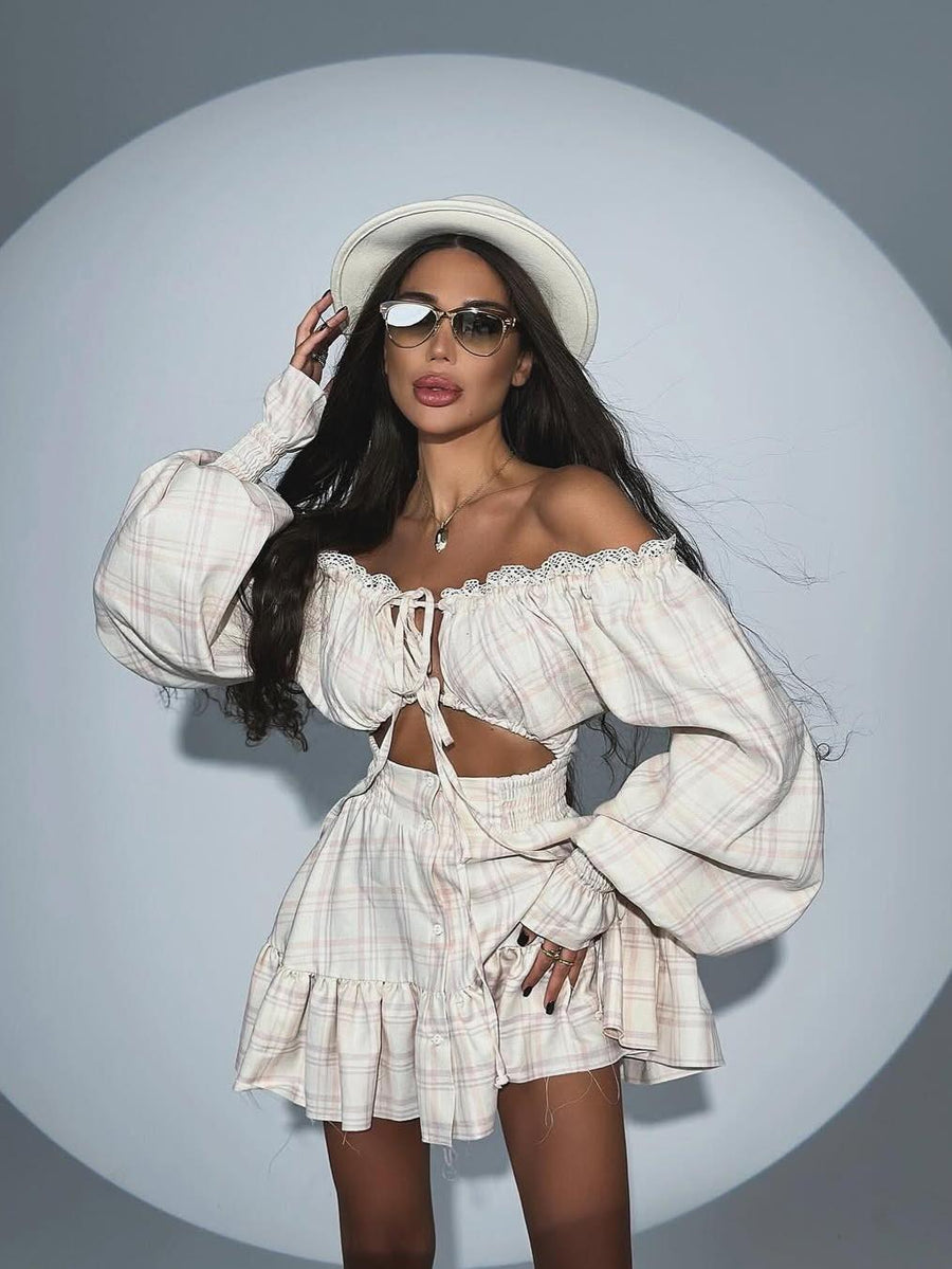 Woman in cream plaid off-shoulder top with lace trim and tie-front, paired with a matching plaid ruffled mini skirt.