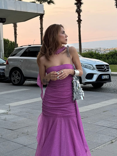 Pink-purple polka-dot strapless dress with an asymmetric ruffle and ruched bodice, draped scarf, and silver clutch.