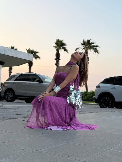 Magenta polka-dot strapless dress with sheer overlay, asymmetric ruffle, and side slit; purple scarf and silver handbag.