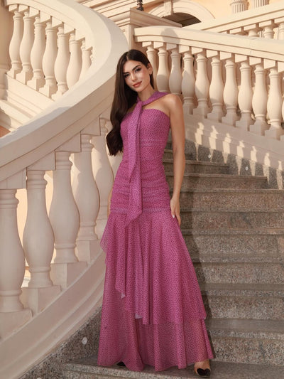 Pink polka dot asymmetric ruffle dress with a neck scarf, model on stone steps beside a curved white balustrade.