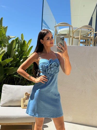 Woman in light blue spaghetti-strap mini dress with large flower applique on bodice and side cutout, outdoors.