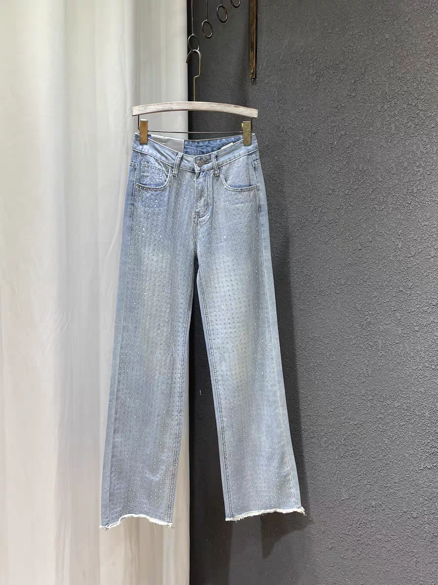 Light-wash blue denim wide-leg pants with rhinestone dot pattern, five-pocket styling and frayed hems, hanging on a wooden hanger.