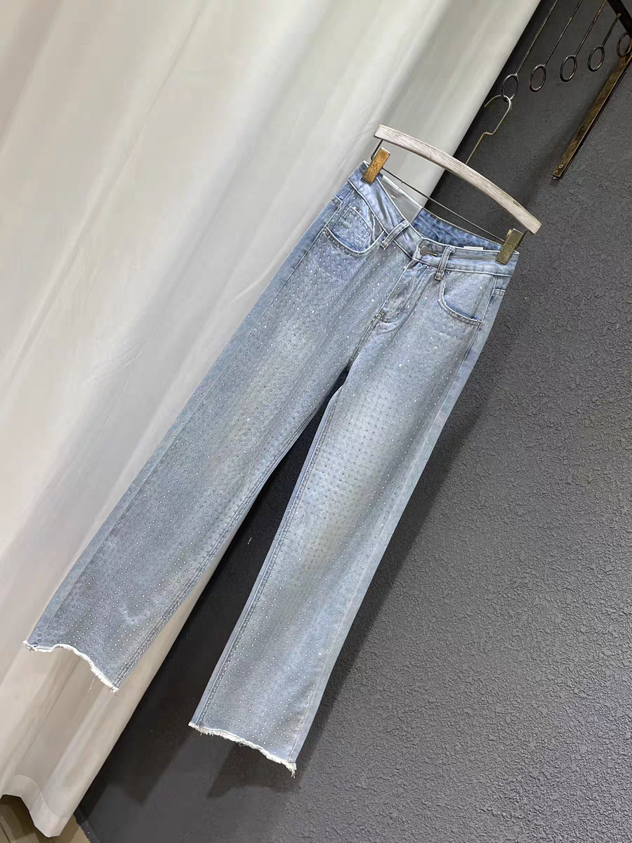 Light blue wide-leg denim pants with scattered rhinestones, frayed hems, five-pocket styling, hanging on a wooden hanger.