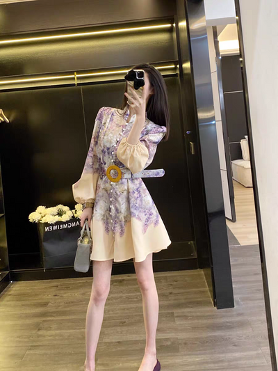Woman posing in a mirror wearing a cream floral short A-line dress with beige puff sleeves and a yellow belt buckle, carrying a gray handbag.