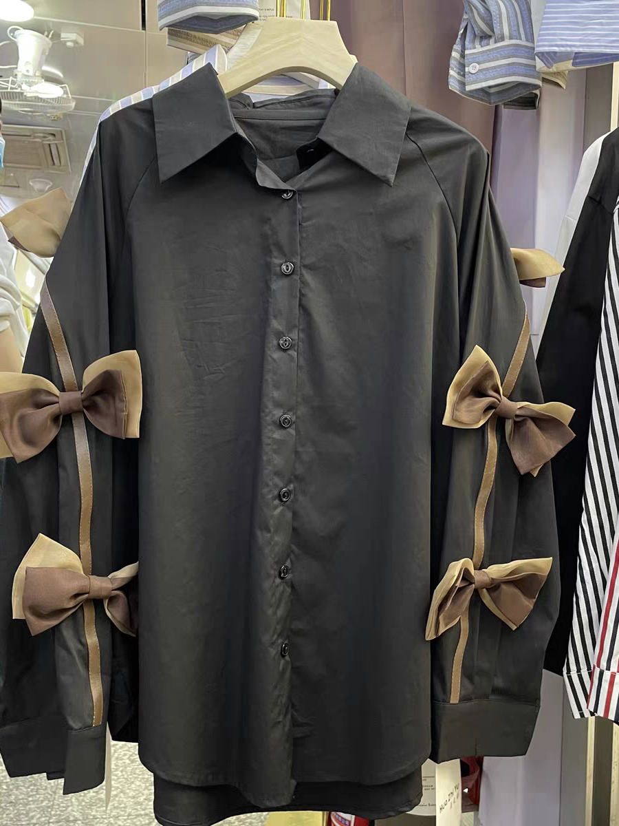 Oversize black button-down shirt with beige ribbon bows along the sleeves.