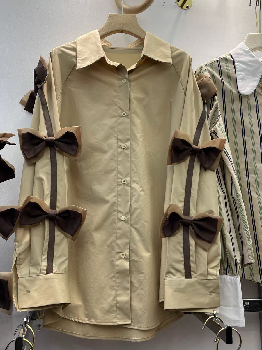 Beige oversized button-down shirt with brown bows on dark ribbons along the sleeves.