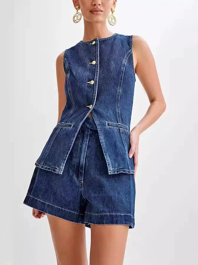 Model wearing sleeveless denim long-vest with gold buttons over matching high-waisted denim shorts in blue wash.