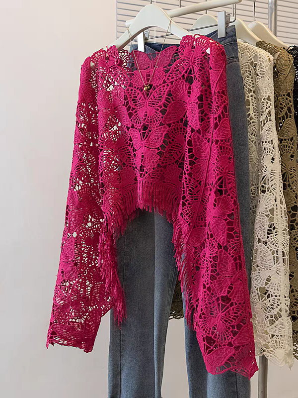 Bright magenta hollow-cut butterfly lace crochet top with fringe hem, hung on a rack beside denim jeans.