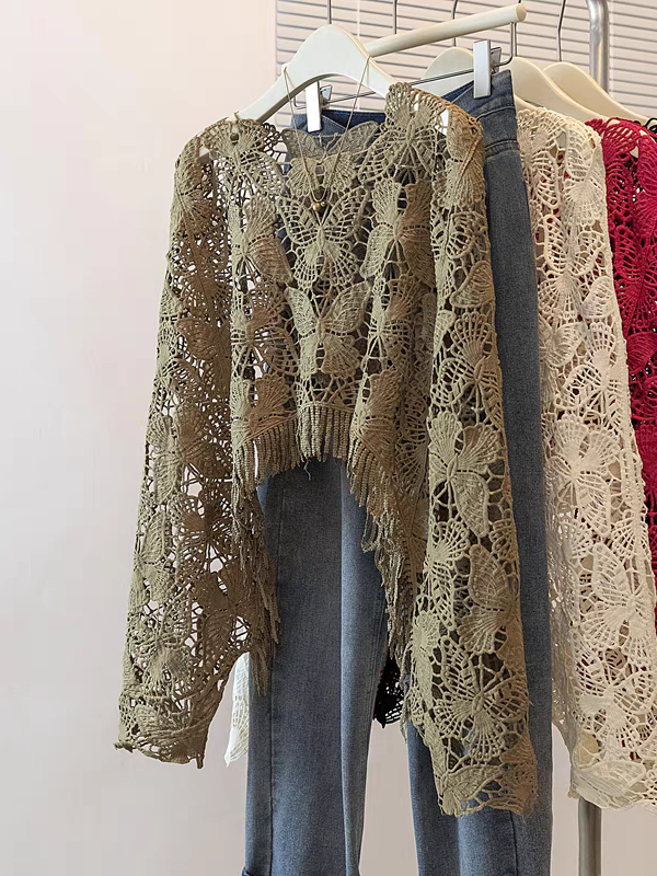 Olive green butterfly-lace crochet top with fringe hem, hanging on a rack among beige and cream lace tops.
