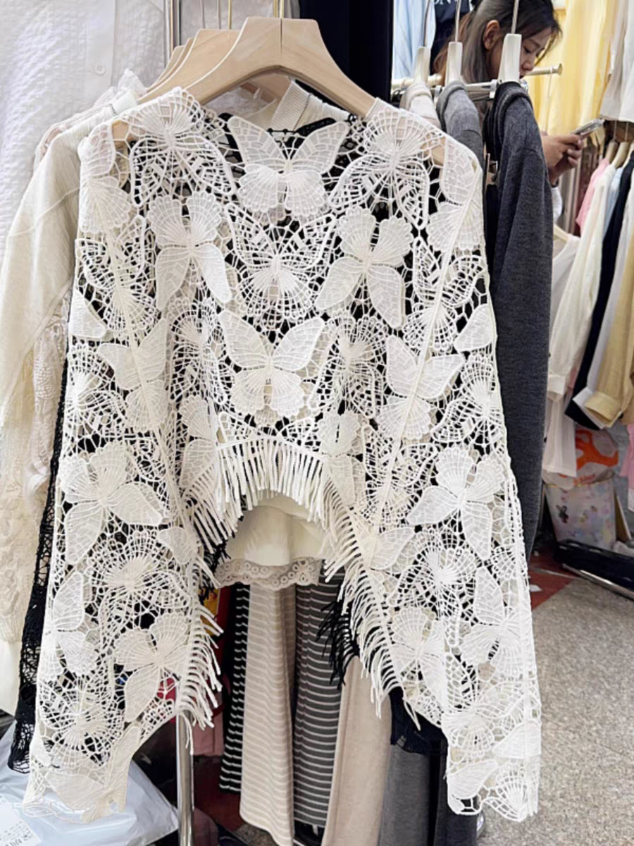 White hollow butterfly lace crochet top with fringe tassels along the hem, on display in a store.