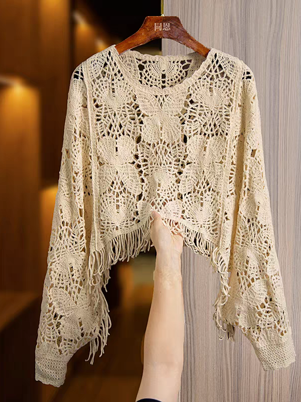 Cream crochet top with butterfly cutouts, long sleeves, and tassel fringe hem, displayed on a wooden hanger.