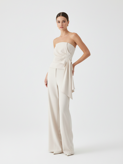 Cream strapless asymmetric tube-top with waist wrap and draped sash, paired with matching wide-leg pants on a model.