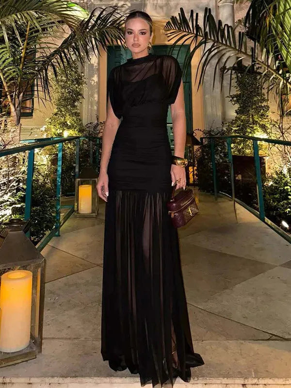 Black sheer-mesh ruched and pleated maxi dress on a woman, opaque bodice with sheer skirt, candlelit garden path.