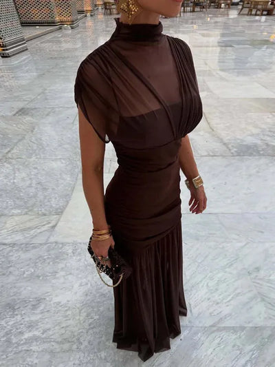 Dark brown sheer mesh ruched pleated maxi dress on a woman with gold jewelry and a beaded clutch.