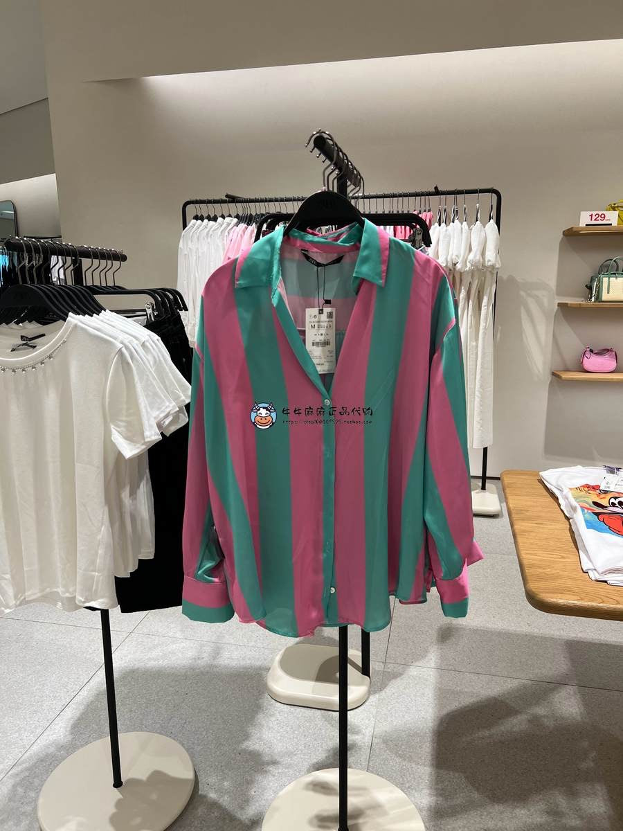 Drop-shoulder satin shirt with pink and teal vertical stripes, collared, on a hanger in a clothing store.