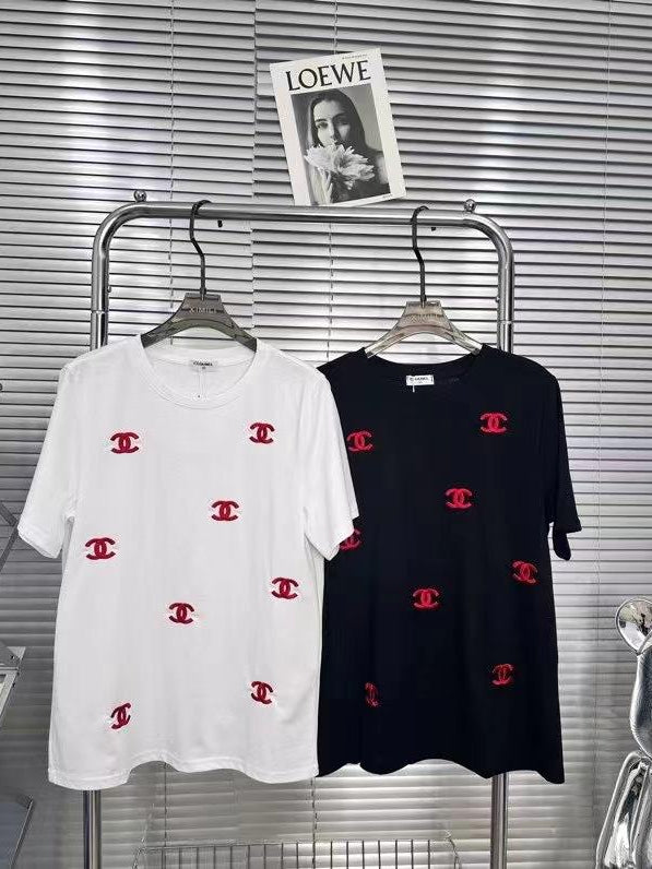 White and black T-shirts with scattered red logos on a metal rack; LOEWE poster above against blinds.